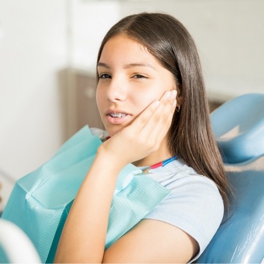 Teen girl in dental chair holding her cheek in pain