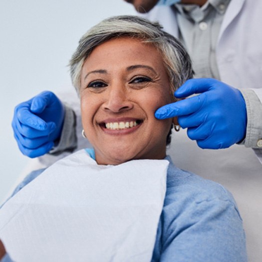 smiling woman looking at her teeth with the dentist behind her