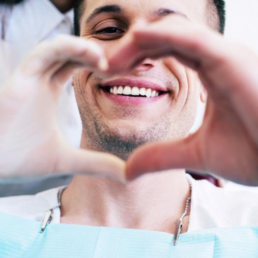 smiling male dental patient making a heart with hands 