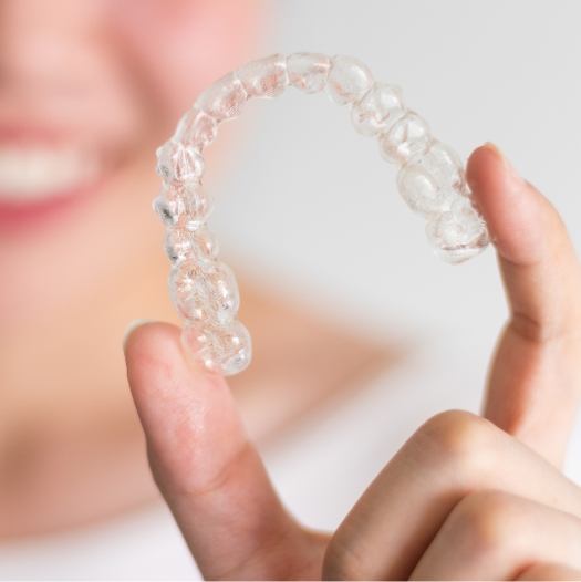 Smiling person holding Invisalign in Dallas