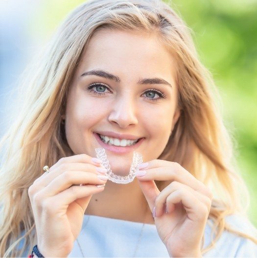 Smiling blonde woman holding an Invisalign aligner