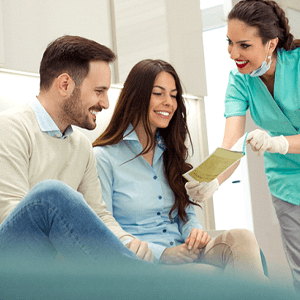 Smiling couple reviewing pamphlet with dental assistant