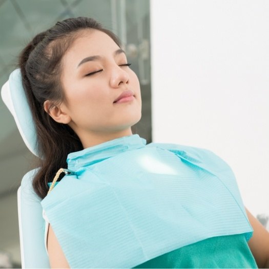 Young woman leaning back in dental chair with eyes closed