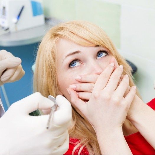 Scared dental patient covering her mouth with her hands