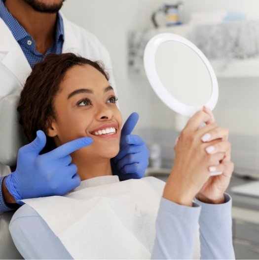 Dental patient admiring her smile in mirror after teeth whitening in Dallas