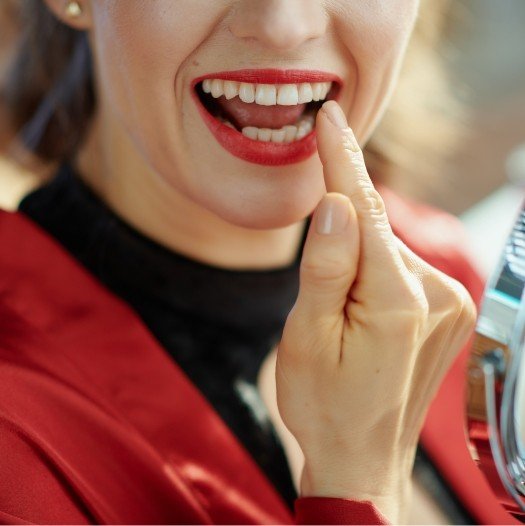 Woman with red lipstick looking at her teeth in mirror