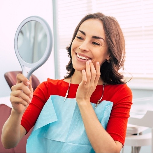 Dental patient in red shirt looking at her smile in mirror